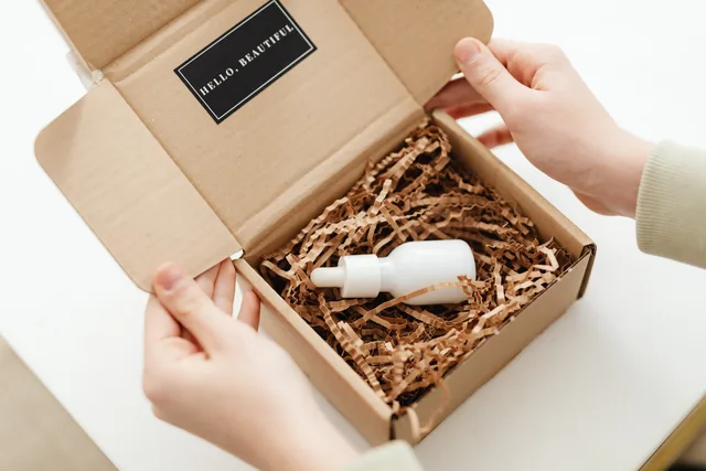 Hands opening a package with a skincare dropper bottle in protective packaging. Launching a direct-to-consumer brand